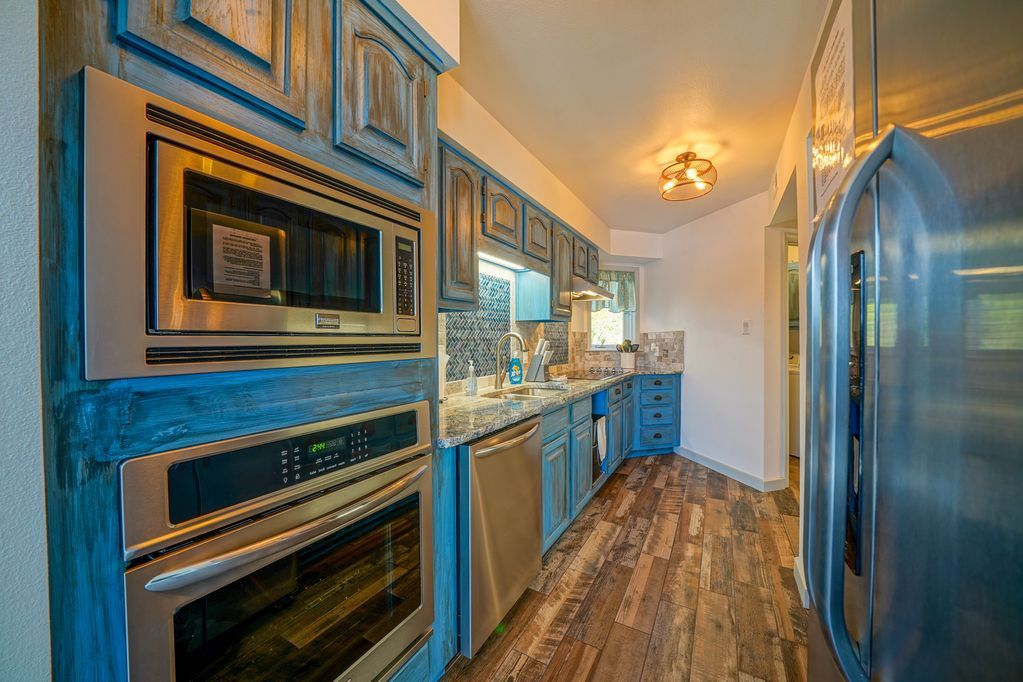 A kitchen with blue cabinets , stainless steel appliances , a refrigerator and a microwave.