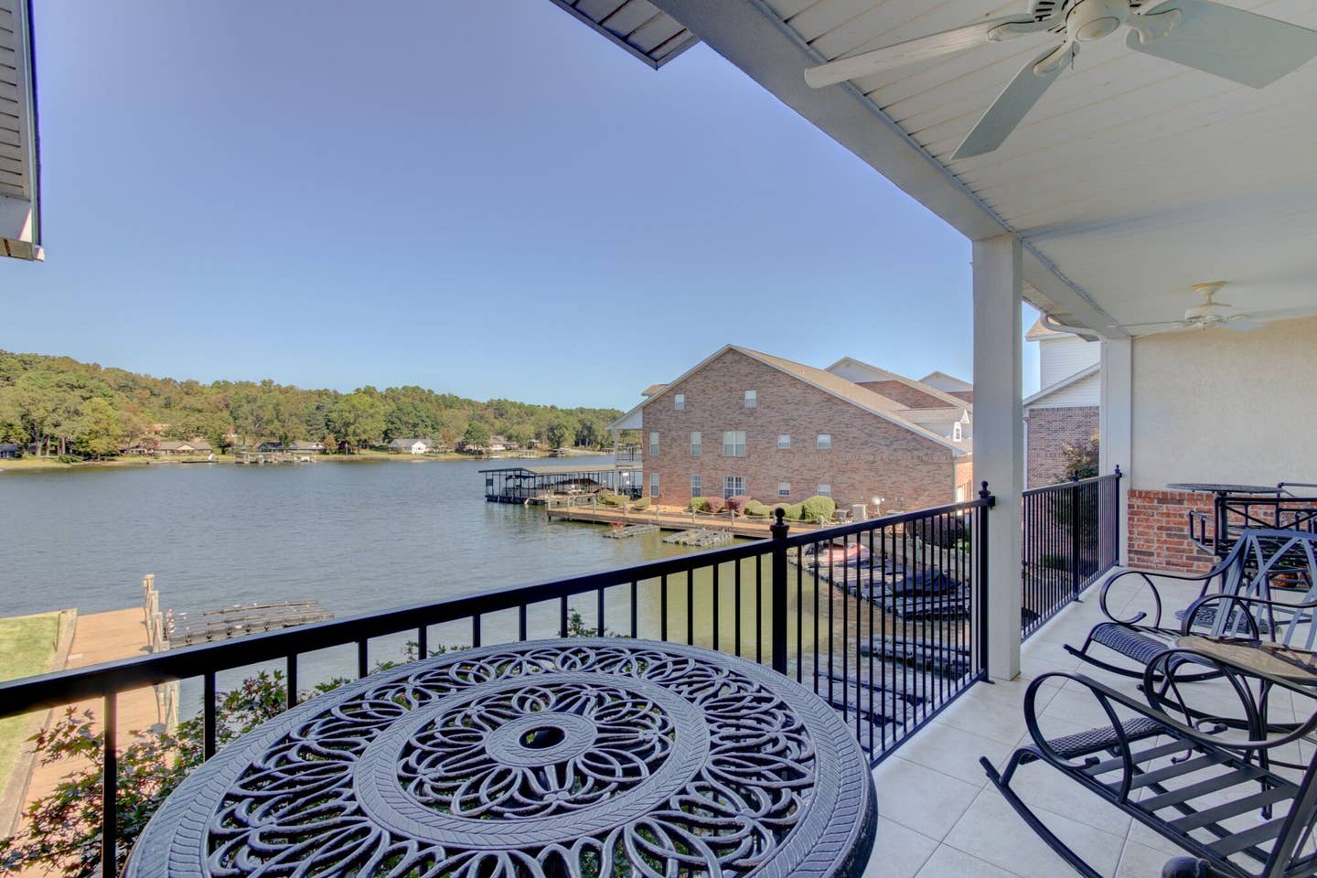 A balcony with a table and rocking chairs overlooking a lake.