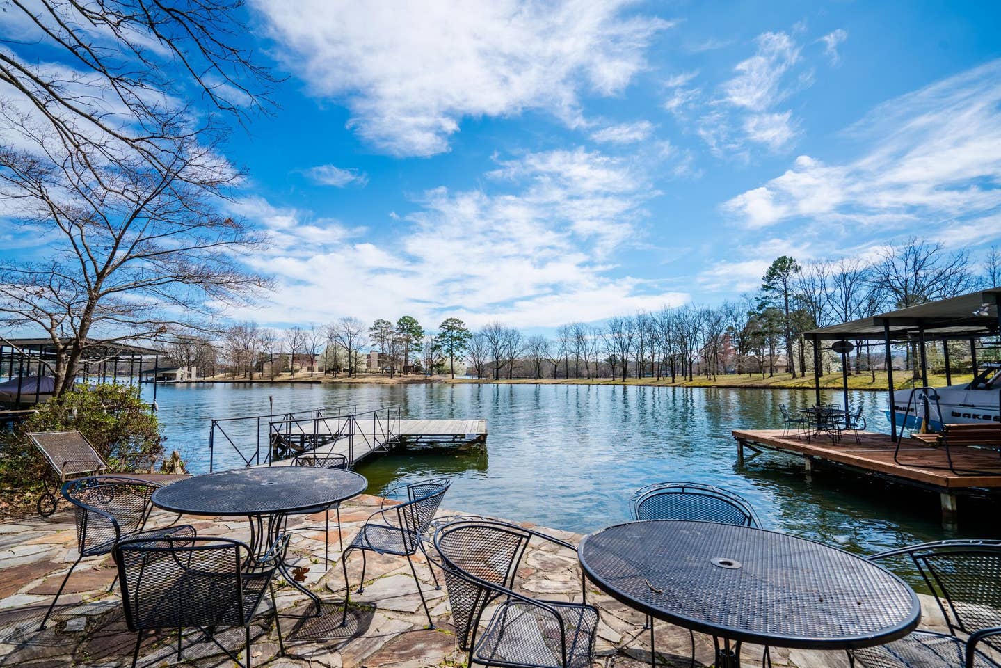 A lake with a dock and tables and chairs on the shore.