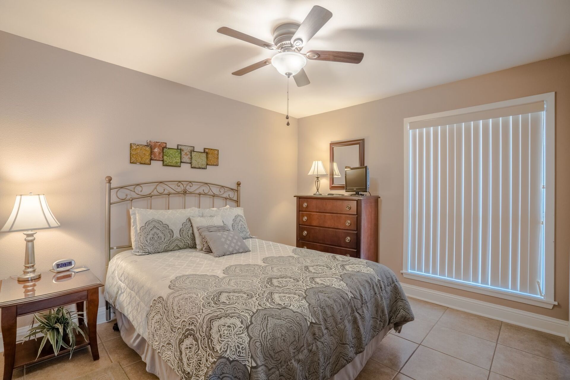 A bedroom with a bed , dresser , mirror and ceiling fan.