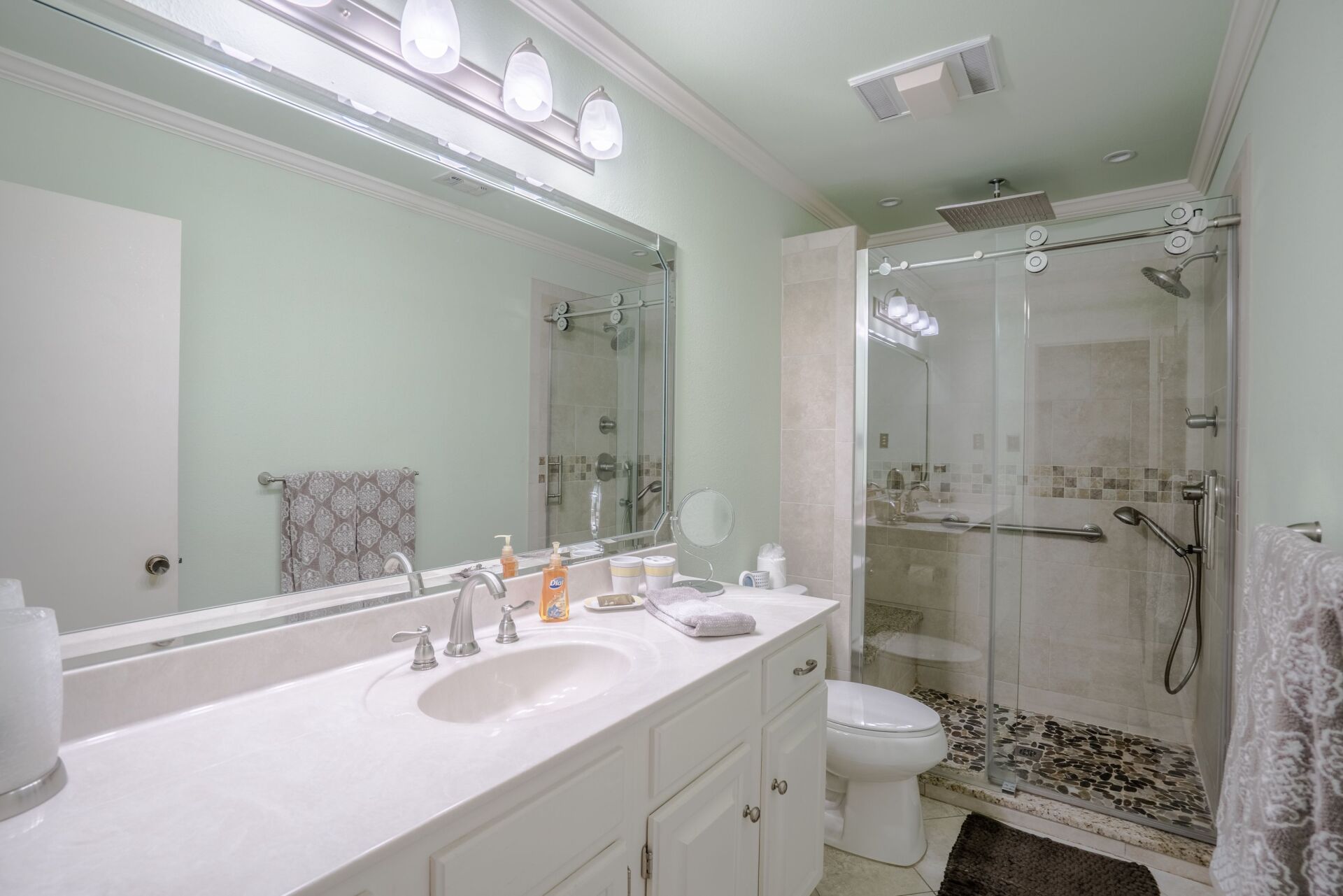 A bathroom with a sink , toilet , shower and mirror.