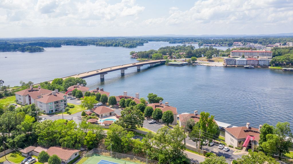 An aerial view of a bridge over a lake with a tennis court in the foreground.
