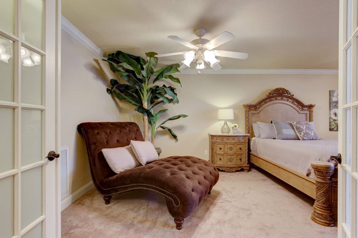 A bedroom with a chaise lounge , bed , nightstand and ceiling fan.