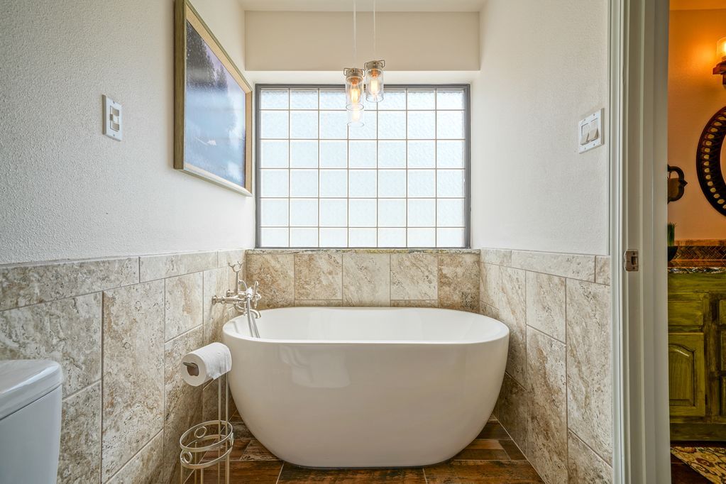 A bathroom with a tub , toilet , and window.