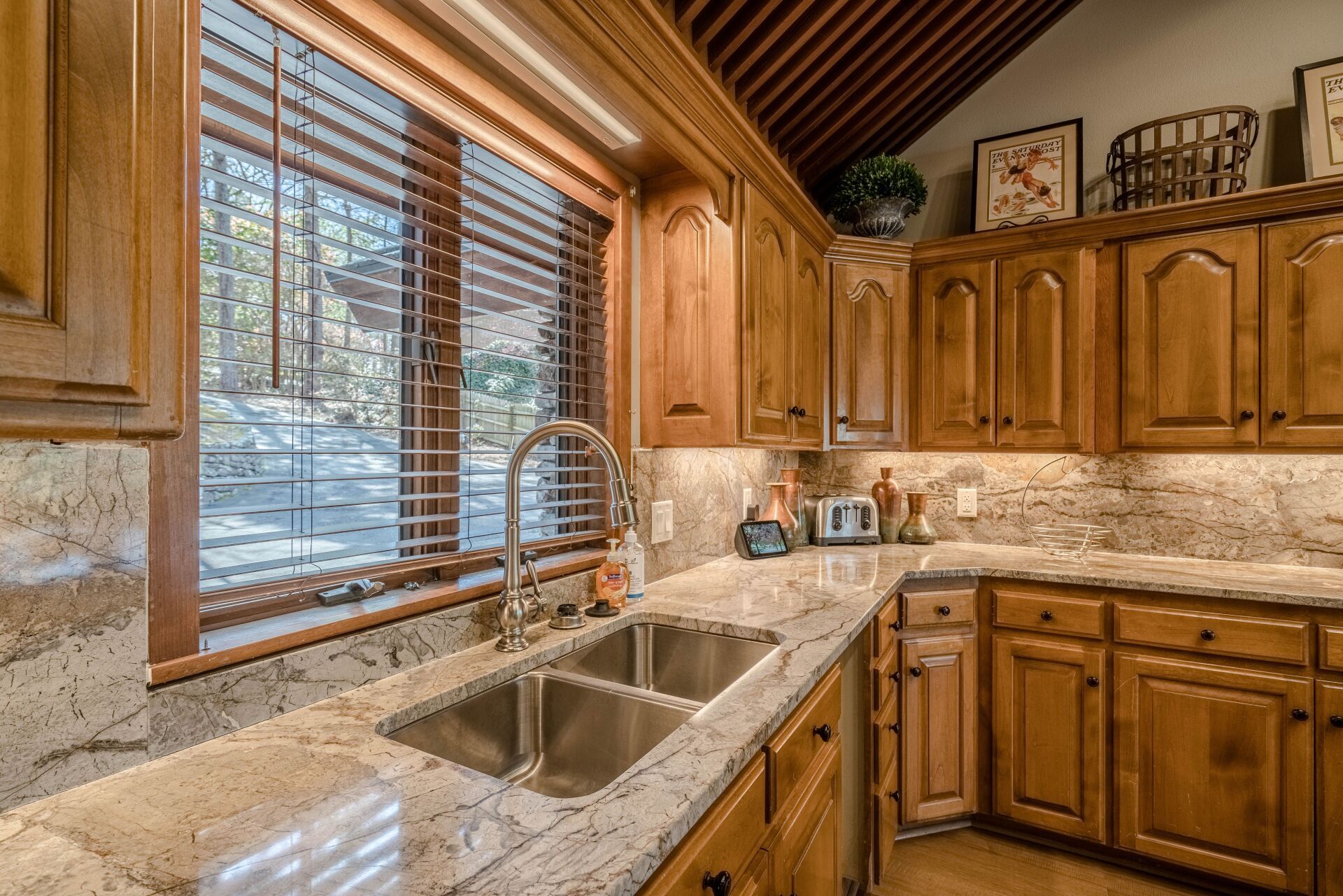 A kitchen with stainless steel sink , granite counter tops , wooden cabinets and a window.