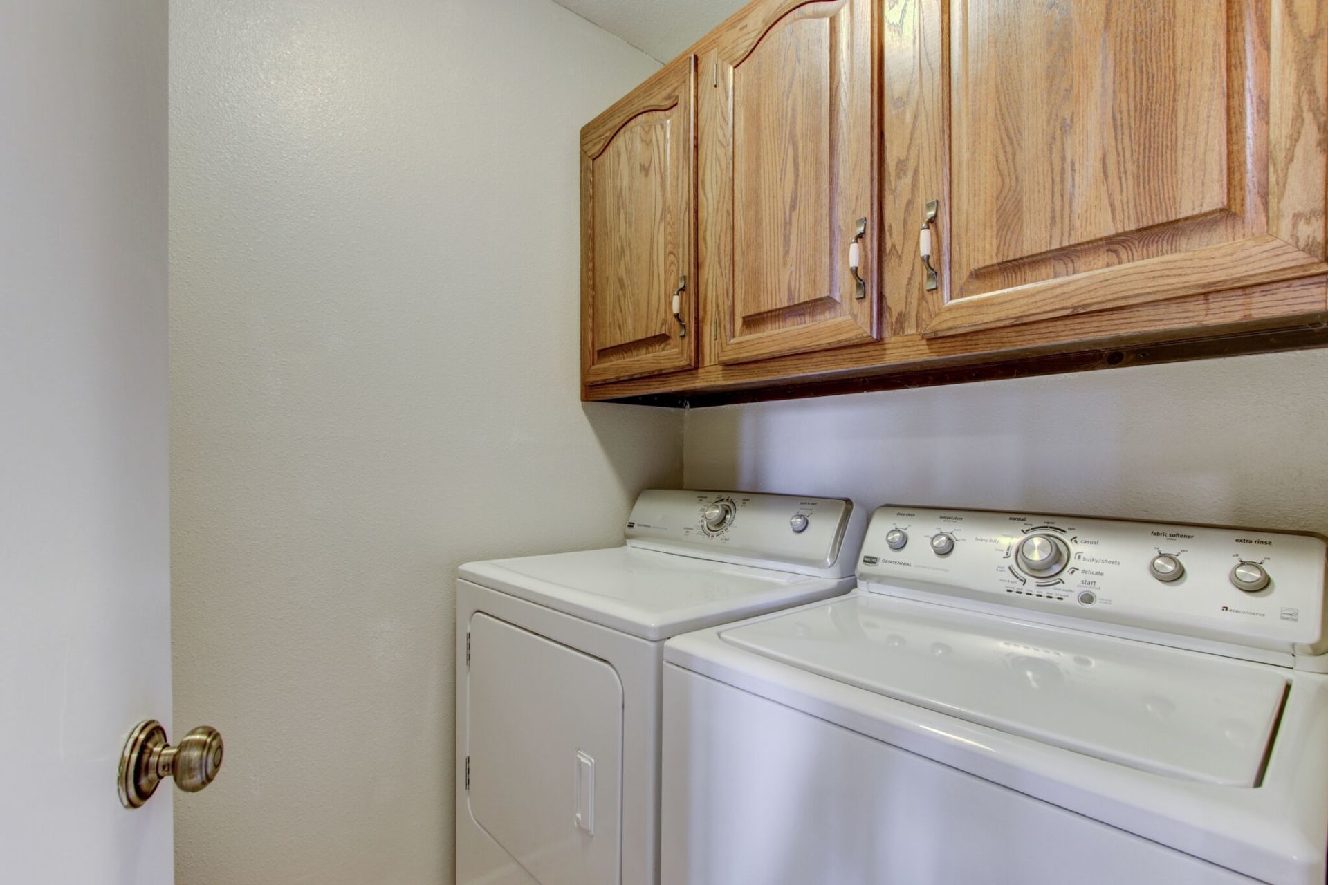 A laundry room with a washer and dryer and wooden cabinets.
