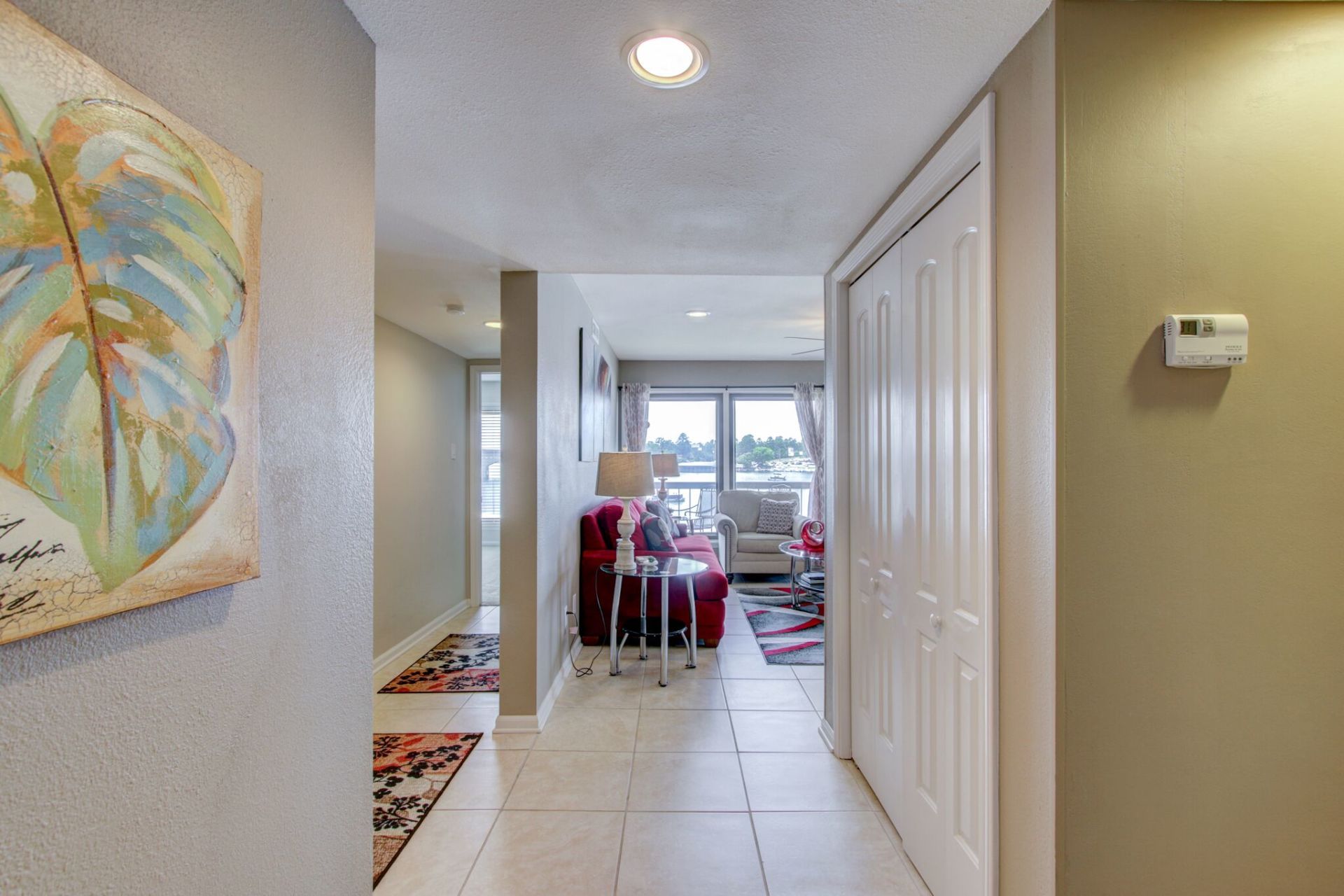 A hallway in a house with a painting on the wall and a thermostat on the wall.