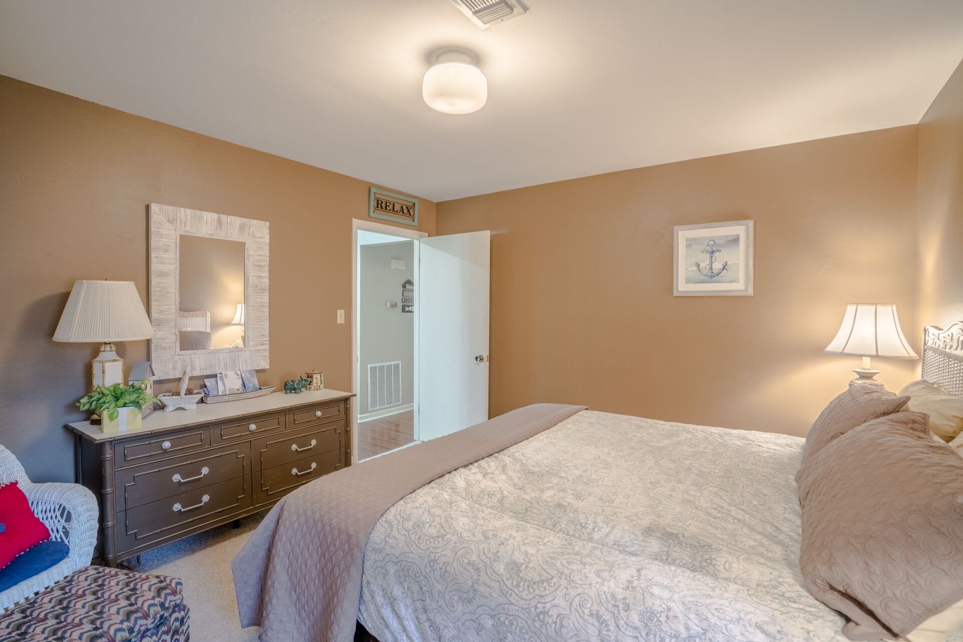 A bedroom with a bed , dresser , lamp and mirror.