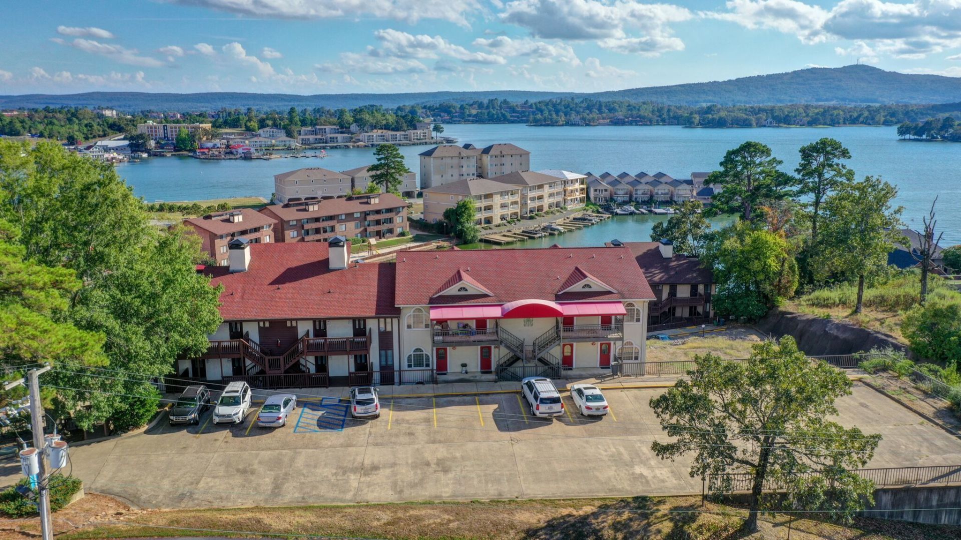 An aerial view of a hotel next to a lake with cars parked in front of it.