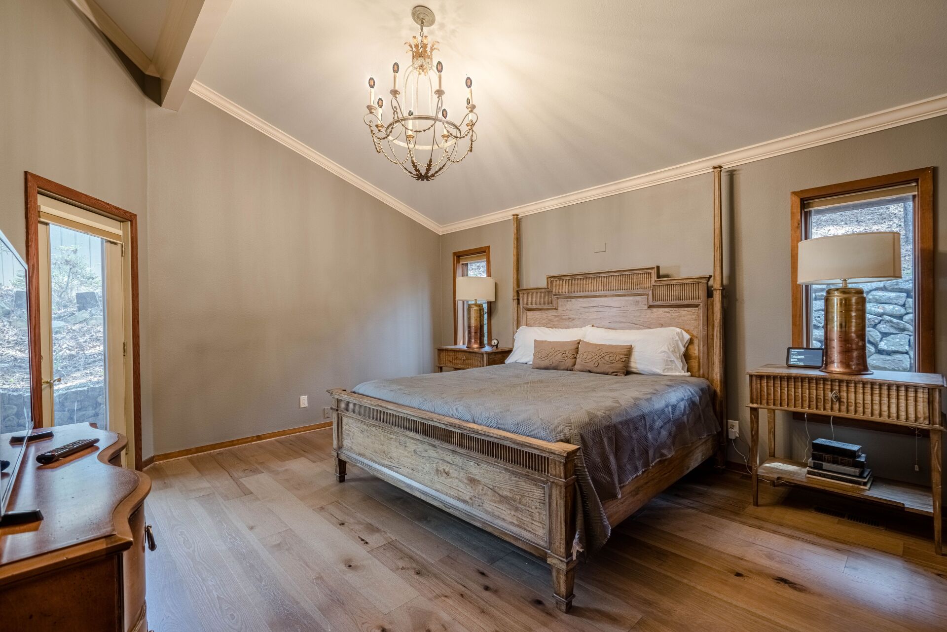 A bedroom with a king size bed , dresser , mirror and chandelier.