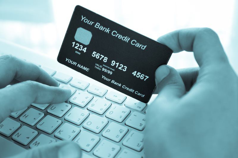 A person holding a bank credit card over a keyboard