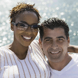 A man and a woman are posing for a picture in front of the ocean.
