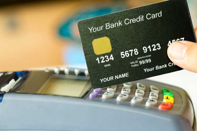 A person is holding a bank credit card over a credit card reader.