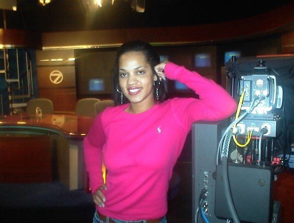 A woman in a pink sweater is standing in front of a camera