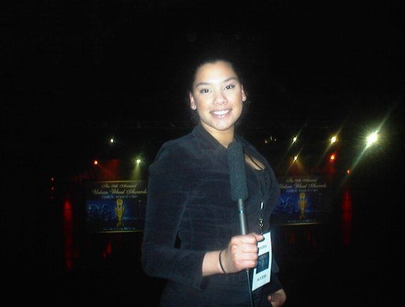 A woman in a black jacket is smiling and holding a microphone