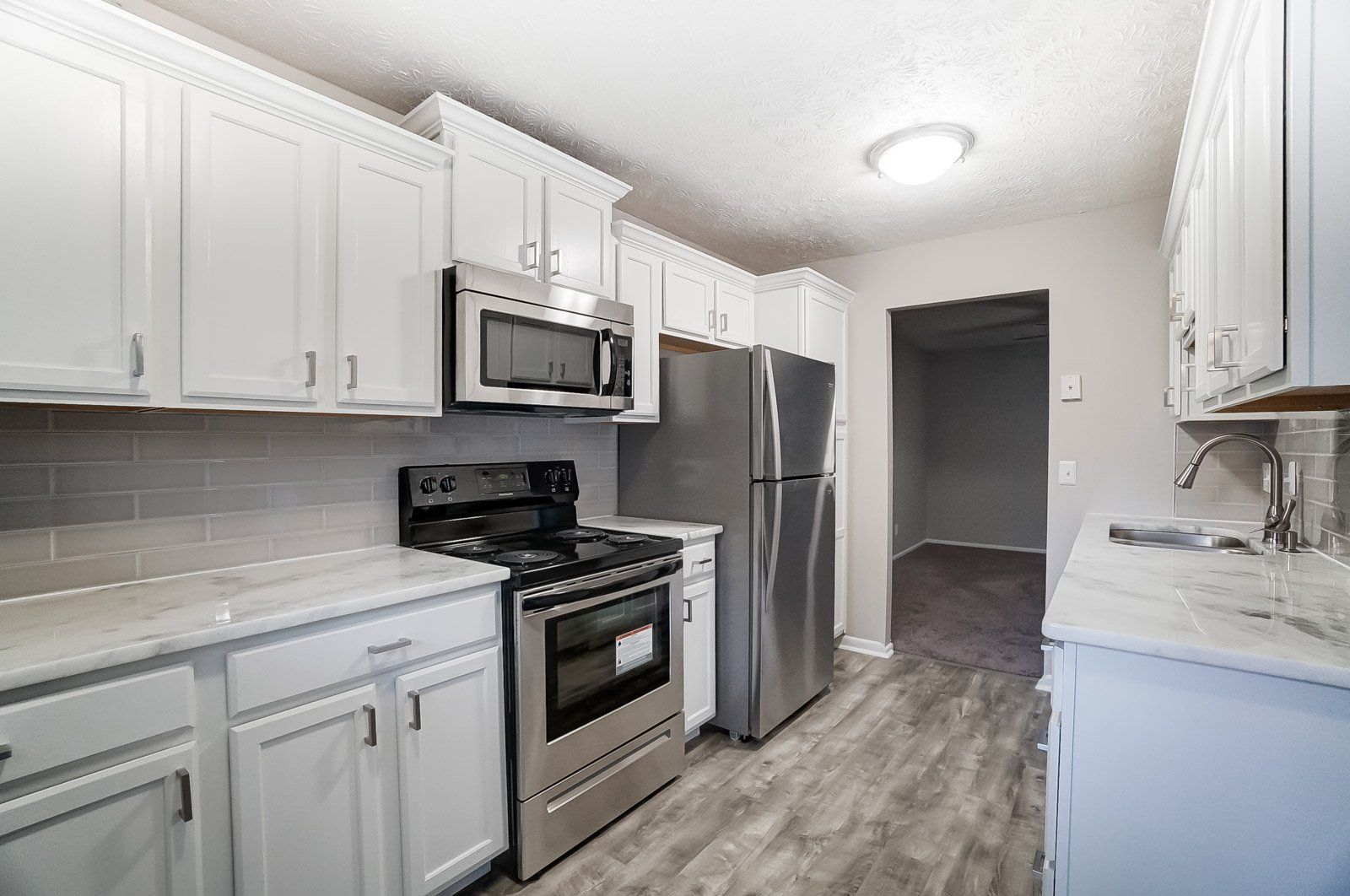 Upgraded apartment kitchen with stainless steel appliances, white cabinets, and wood-style flooring.