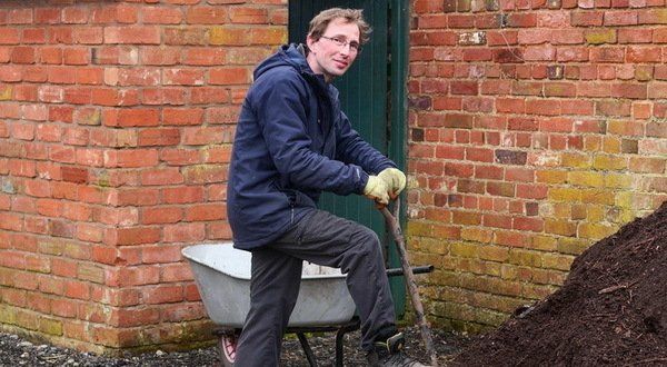 A man is sitting on a wheelbarrow next to a pile of dirt.