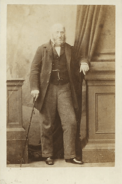 A man with a cane is leaning against a wall in a black and white photo.