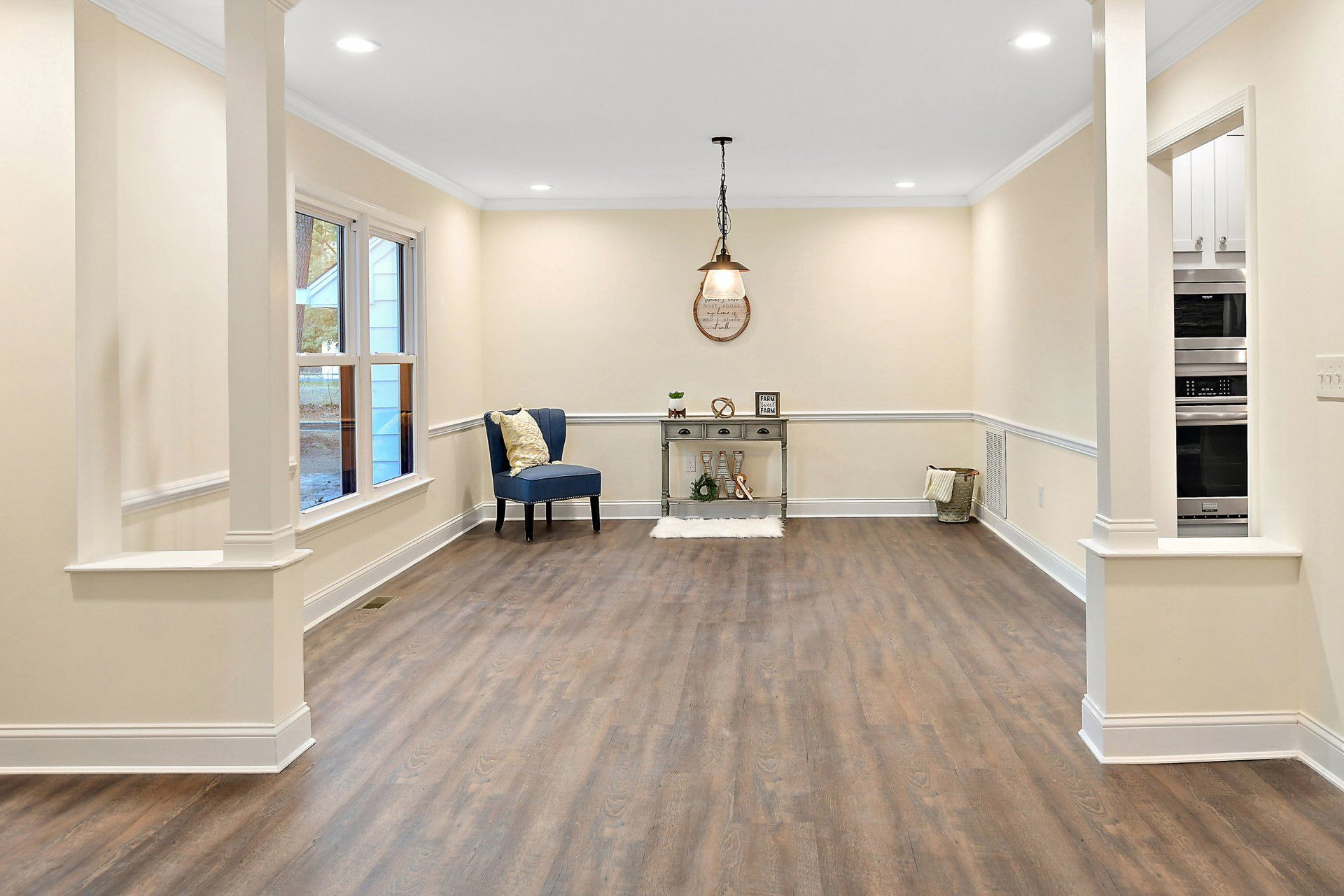 Spacious dining room with wood flooring, pillars, chair, table, and light fixture.