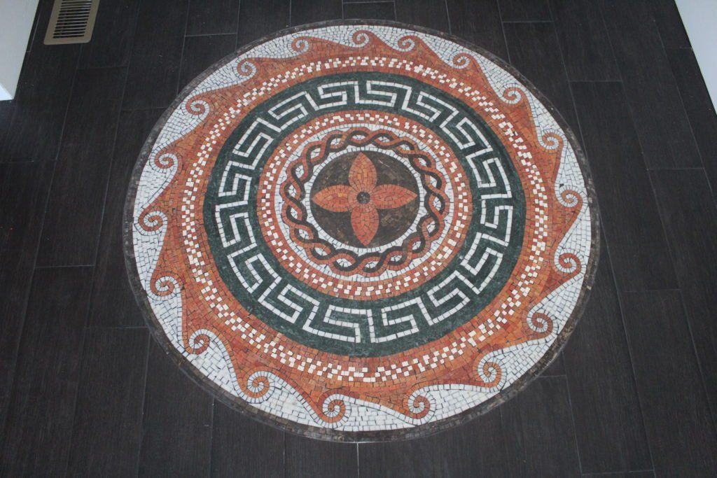 Circular mosaic floor design featuring a flower in the center, surrounded by patterns and borders.