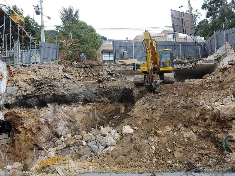 Una excavadora amarilla está cavando un hoyo en un montón de tierra.