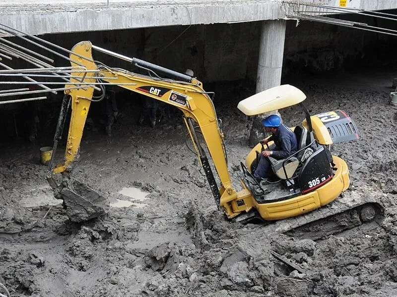Un hombre conduce una excavadora amarilla en el barro.