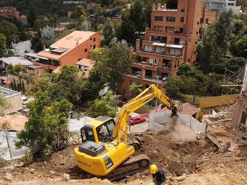 Una excavadora amarilla está moviendo tierra frente a un edificio.