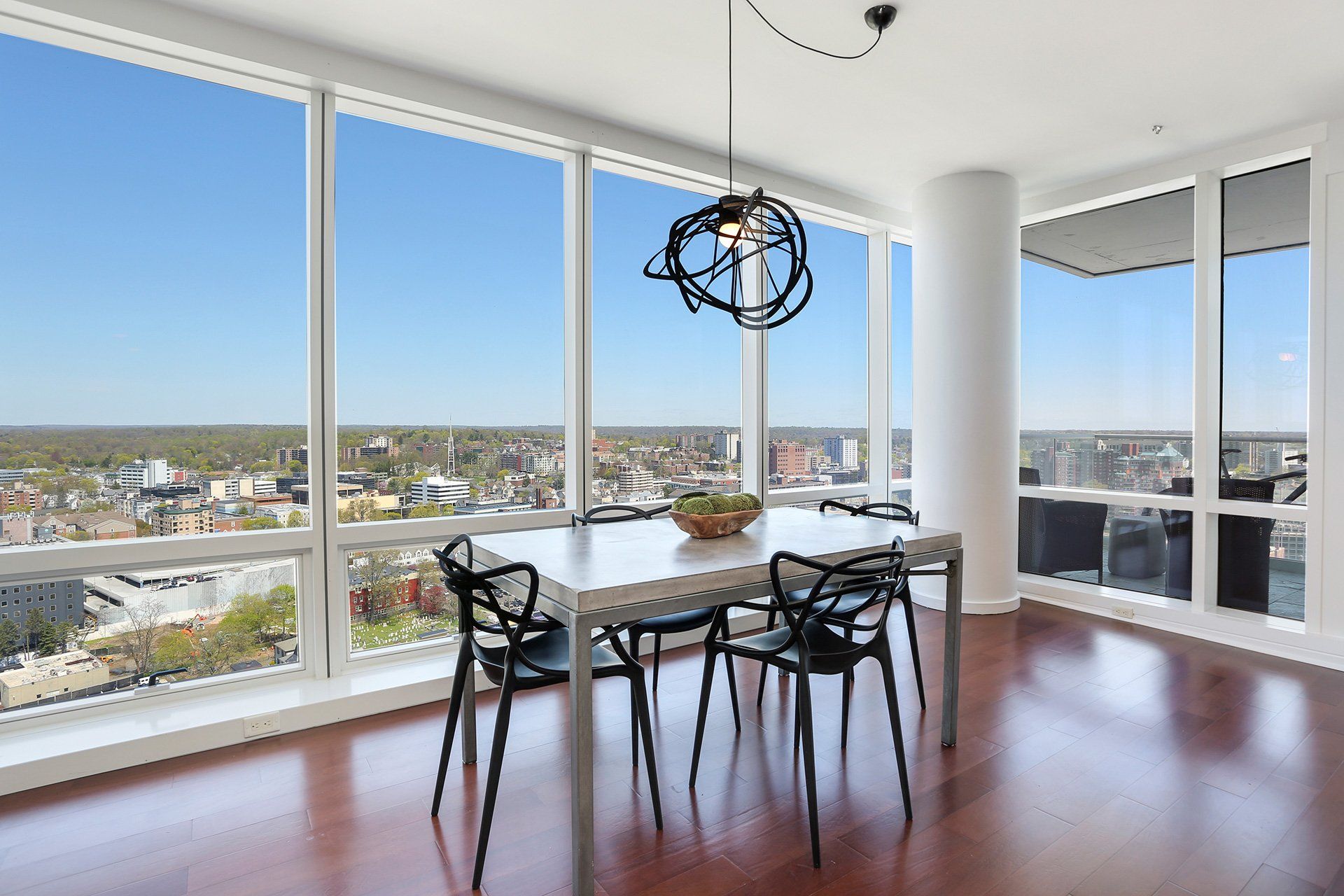 Dining room with cityscape view; large windows, white table, black chairs, modern light fixture.