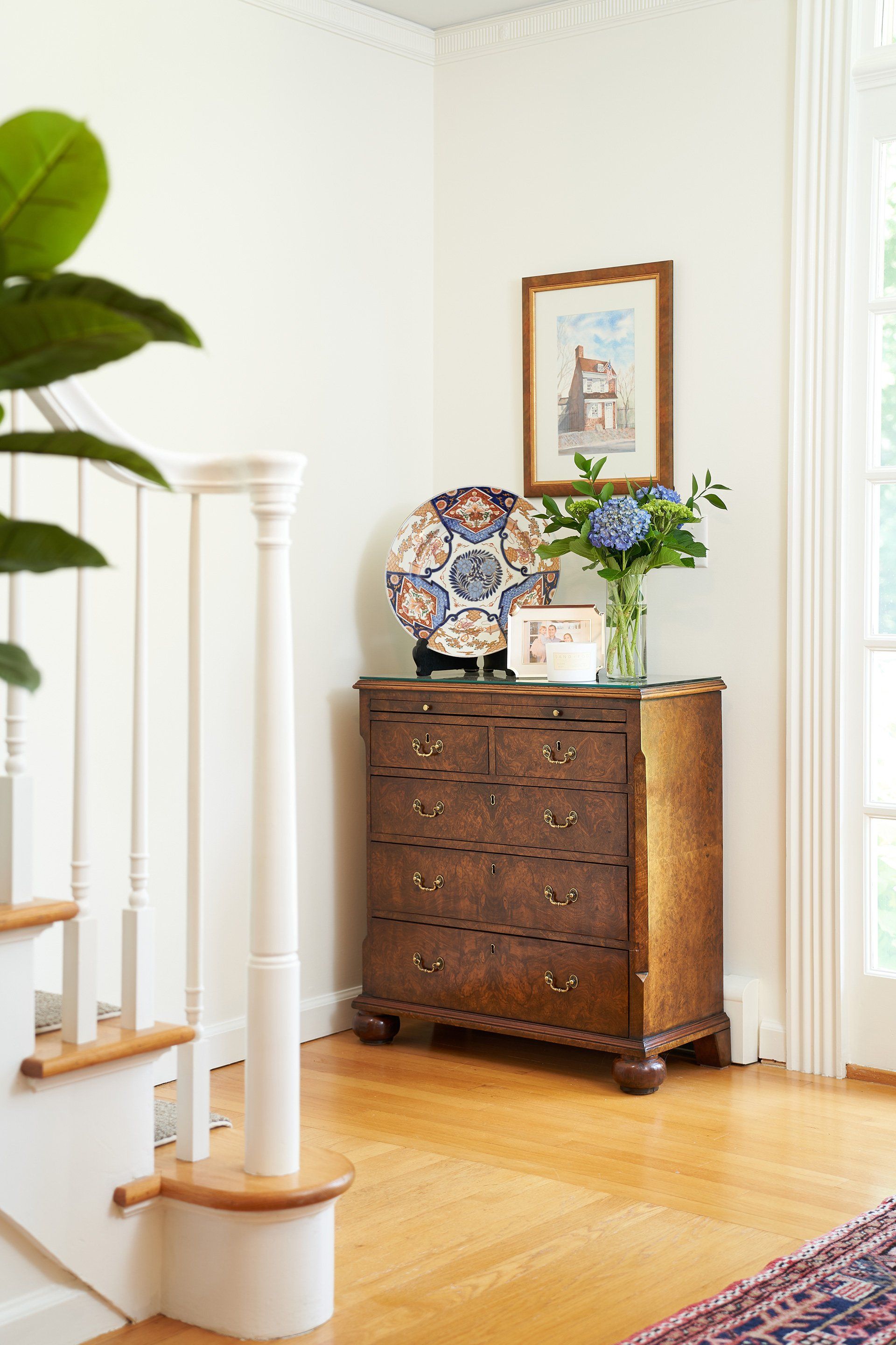 Wooden chest with decorative items in a bright entryway with a staircase and window.