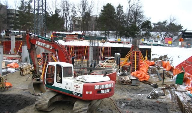 Red excavator at a construction site with concrete forms and snow in the background.