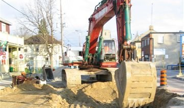 Excavator digging in a construction zone next to buildings.