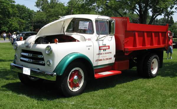 White and red vintage dump truck with green accents parked on grass with hood open.