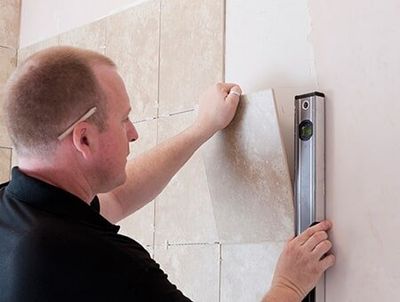 A Tiler Lining Up A Tile To Place On The Wall — Remodeling Contractor in Denver, CO A Tiler Lining Up A Tile To Place On The Wall — Remodeling Contractor in Denver, CO