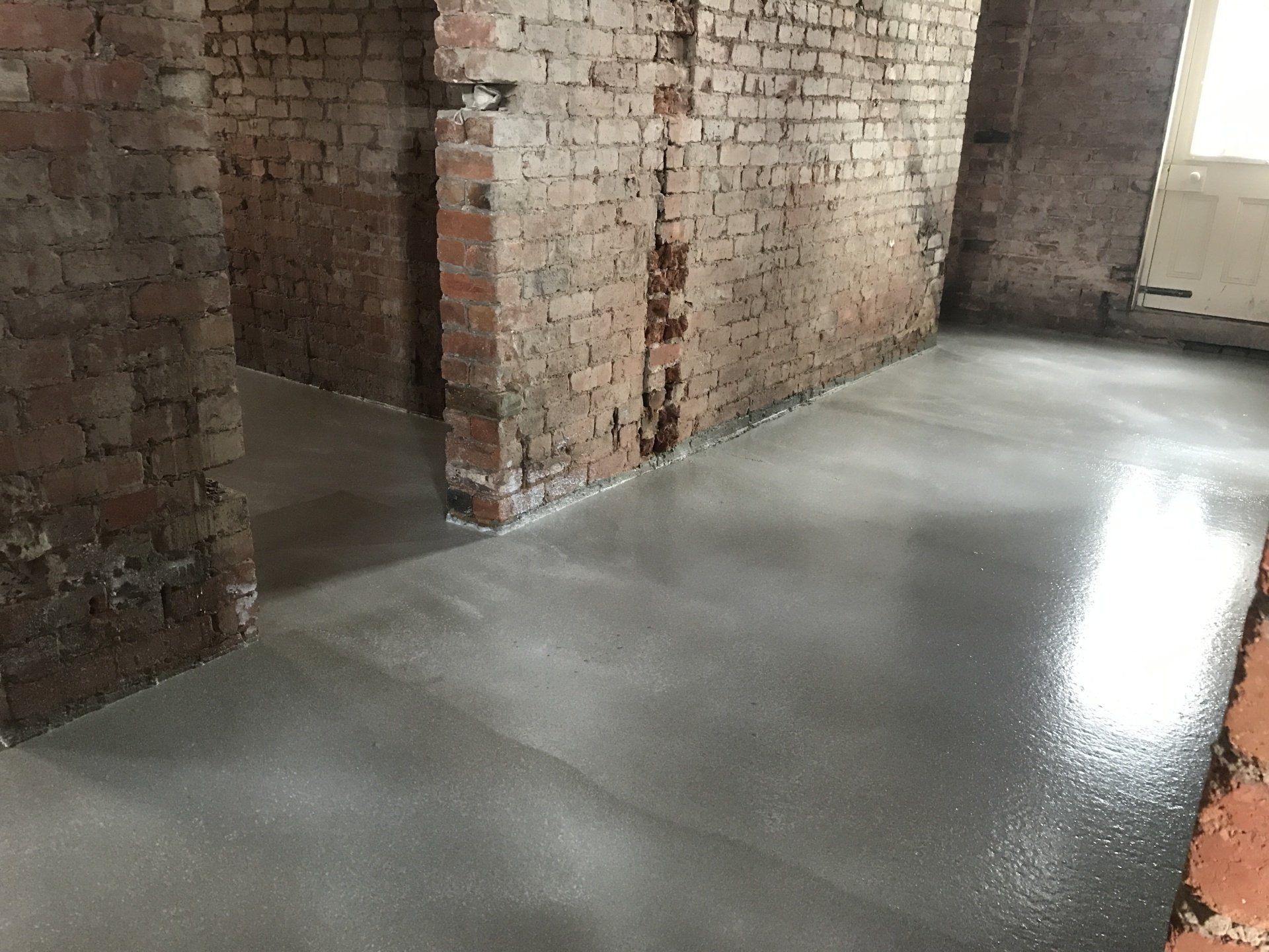 Empty brick interior with a smooth gray concrete floor and light from windows.