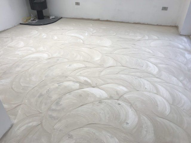 Freshly smoothed white floor in an empty room with swirling trowel marks and gray walls.