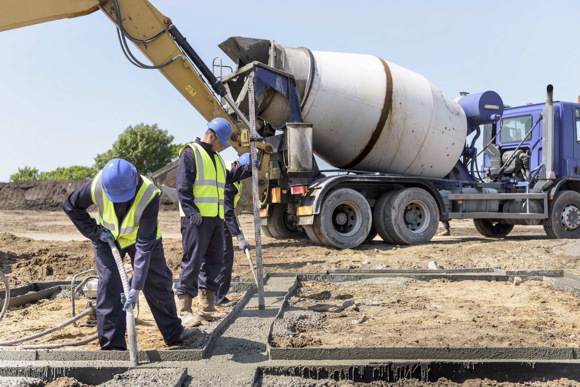 Construction workers in hard hats inspecting concrete at a building site beside a cement mixer truck