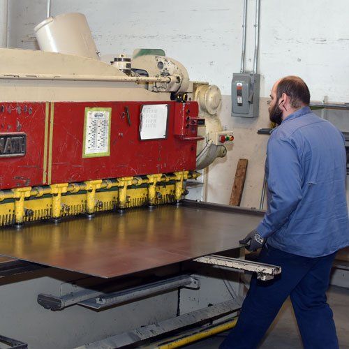Worker guiding a large red industrial machine with yellow clamps in a workshop