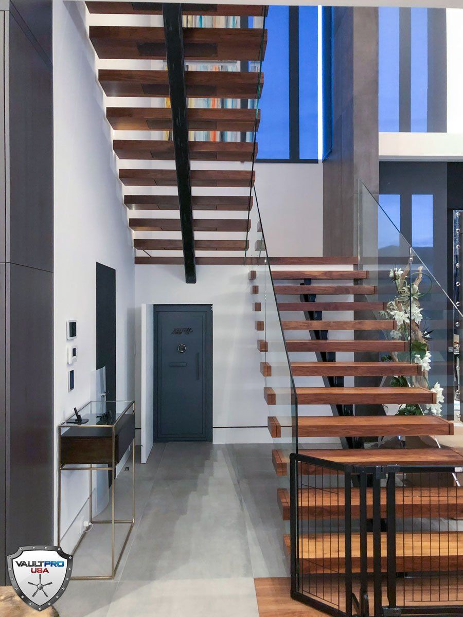 Hidden vault door under a wooden staircase in a modern house with a glass railing