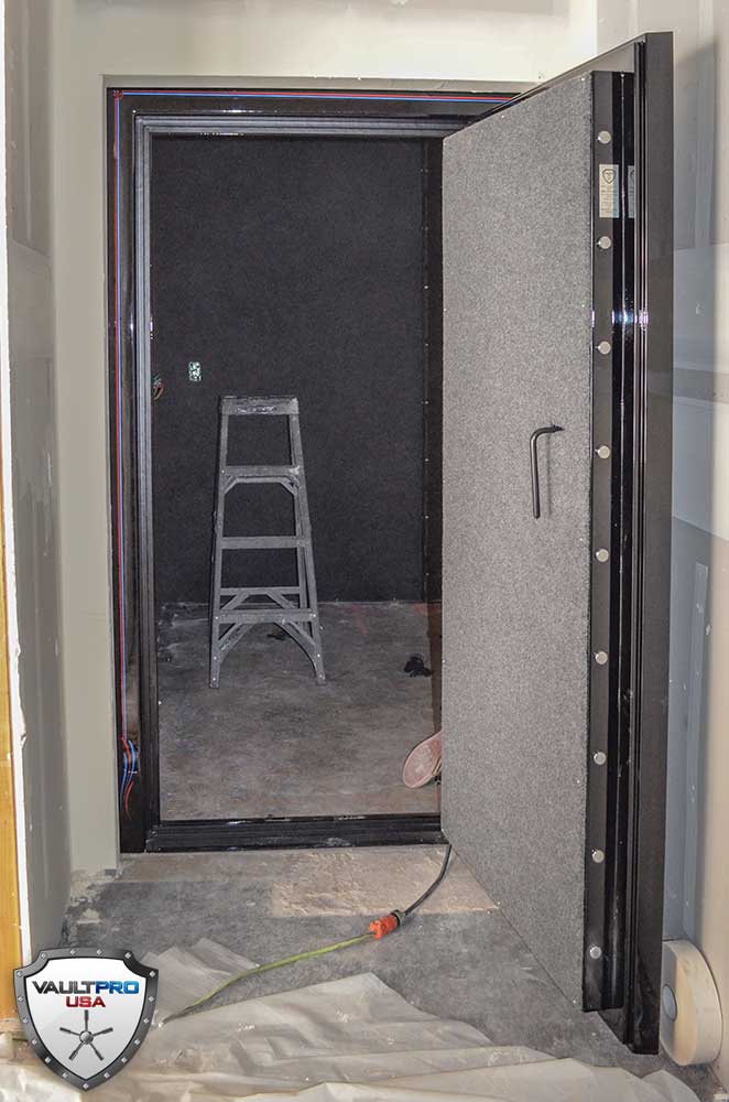 Open black security door revealing a dark room with a step ladder inside and a plastic sheet on the floor