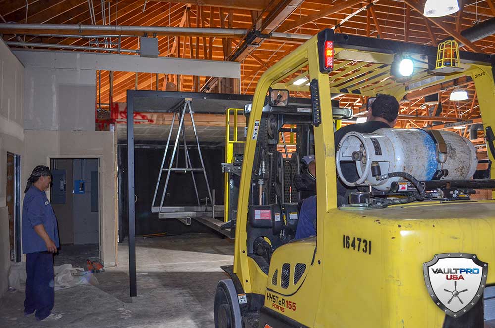 Yellow forklift in an industrial workshop beside a hanging metal frame and a man standing nearby