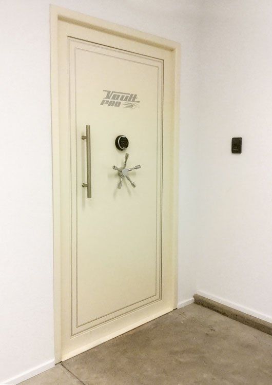 Cream-colored vault-style door with a round handle in a plain room with beige carpet.