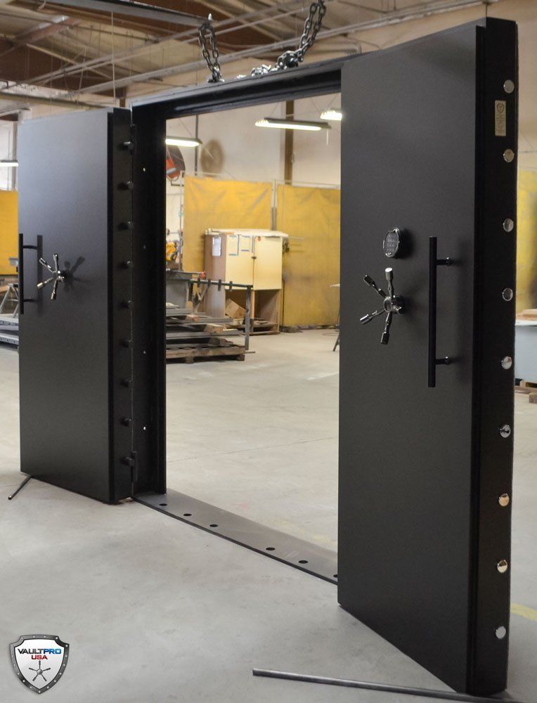 Open black bank vault door in an industrial room, revealing a workshop inside.