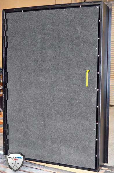 Large gray padded panel or door with a black frame and yellow handle, standing upright indoors.