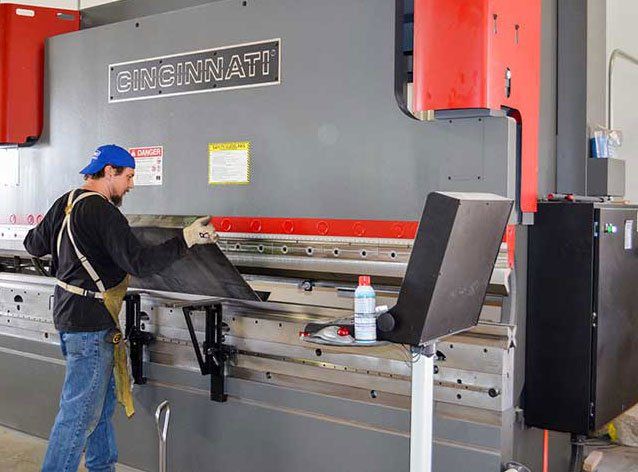 Worker operating a large Cincinnati press brake in a workshop, with red and gray machine panels.