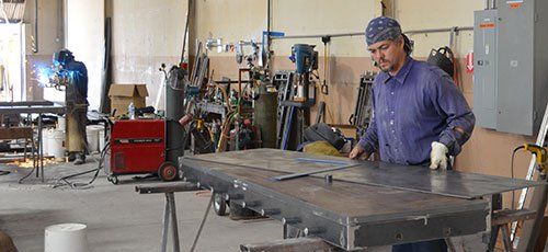 Worker in a workshop operating a large metal sheet on a table with tools and equipment around.