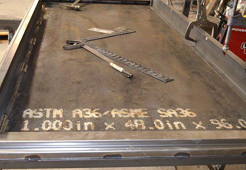 Metal fabrication table with measuring tools and chalk markings on a steel plate