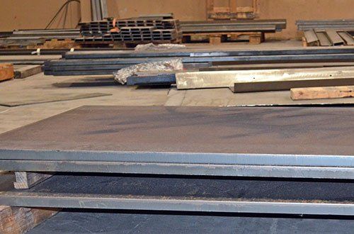 Stacks of large metal sheets and wooden planks in a warehouse-like storage area