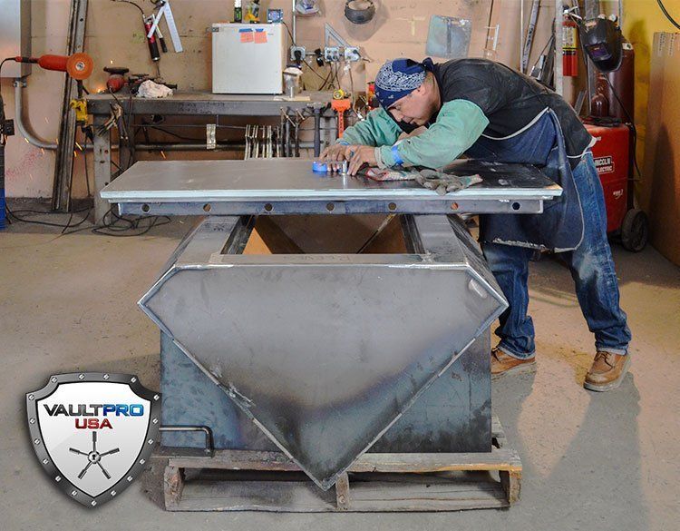 Worker welding a large metal hopper in a workshop, wearing a blue cap and green gloves.