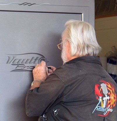 Man in a black jacket sign-paints a gray garage door with the word “Vault.”