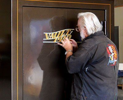 Man in a black jacket signing a gold logo on a dark door